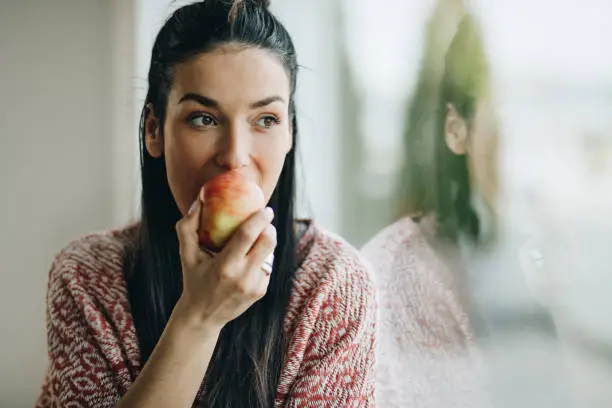 Photo of Pensive woman eating an apple by the window.