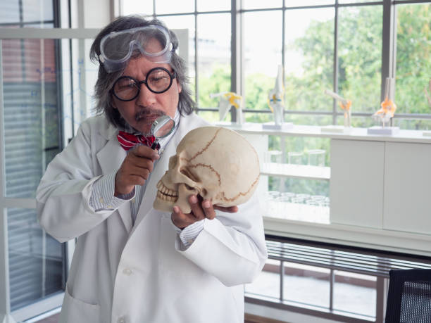 istock asian doctor with a magnifying glass and skull in hand 1073708430