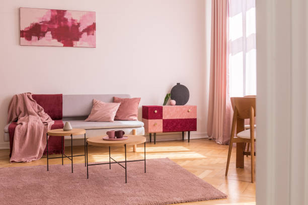 istock Poster above grey sofa with pillows in bright living room interior with table on pink carpet. Real photo 1073712754