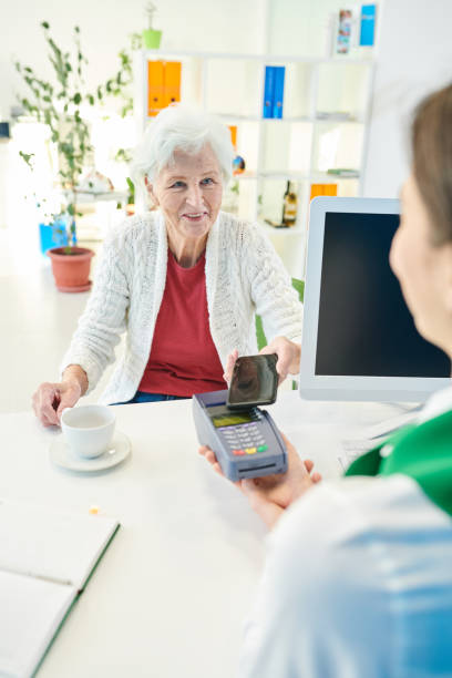 istock Senior bank client drinking coffee while paying with smartphone 1073714816