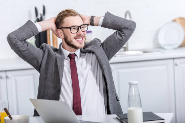istock smiling businessman with hands on head sitting at kitchen table and using laptop during breakfast 1073715658