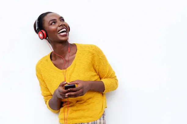 Photo of smiling young african woman listening to music with headphones and mobile phone against isolated white background