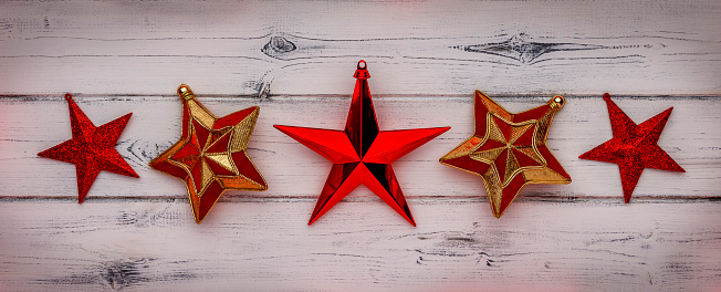 A row of red star christmas decorations, on a distressed white wooden background.
