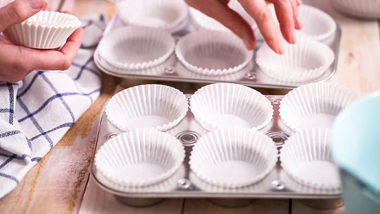 Lining metal muffin pan with paper cupcake liners to bake blueberry muffins.