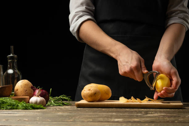 istock The chef cleans potatoes for mashed potatoes, stews, roasted and with vegetables. For dishes with potatoes. On a black background, the concept of the menu, cooking, healthy eating 1073724292