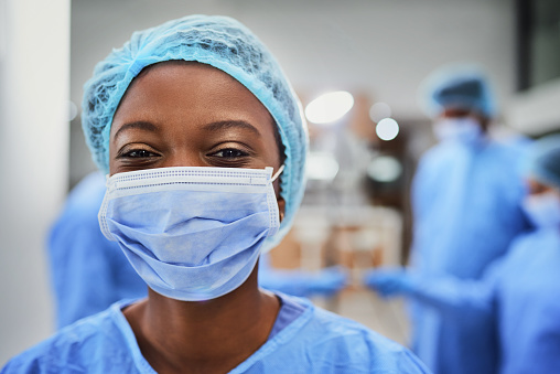 Cropped portrait of a young female nurse standing in the OR with her colleagues in the background