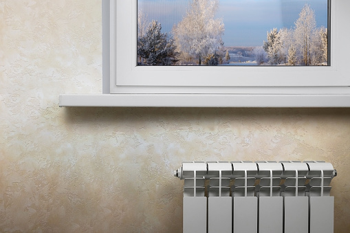 White sectional heating radiator under a white window. The image has an empty space for the inscription.