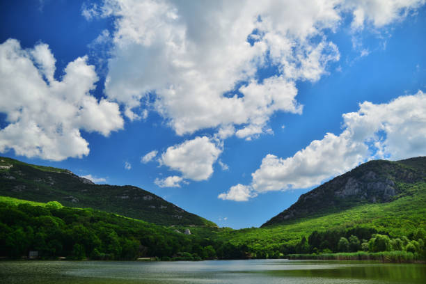 Quiet lake in the green mountains on a background of blue sky with clouds