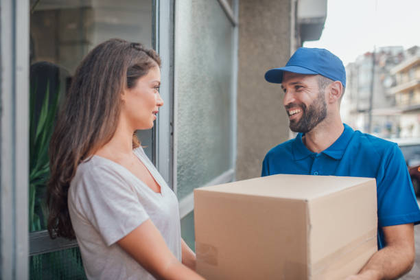 istock Smiling postal worker delivering a package to young woman 1073738780