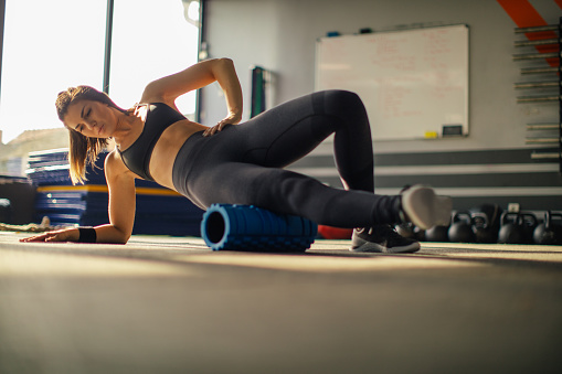 Young muscular woman using foam roller for stretching muscles after hard weightlifting training