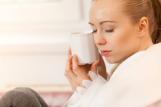 istock Woman lying on sofa under blanket drinking tea 1073744494