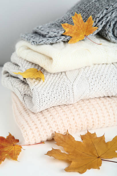 istock Stack of folded sweaters and scarf with autumn leafs on gray background 1073755688