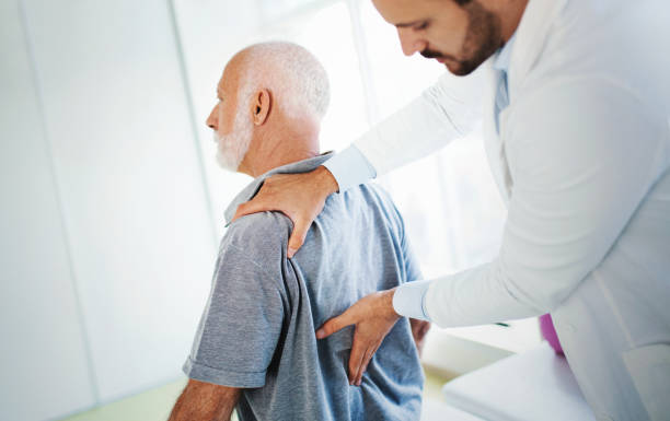 Lower back pain medical examination. Closeup side view of an early 60's senior gentleman having some lower back pain. He's at doctor's office having medical examination by a male doctor. The doctor is touching the sensitive area and trying to determine the cause of pain. herniated disc stock pictures, royalty-free photos & images