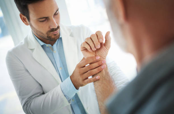 Wrist injury. Closeup of a mid 30's doctor examining a senior male patient with injured wrist. The doctor is slowly moving and rotating patient's hand in order to determine the exact cause. rheumatoid arthritis stock pictures, royalty-free photos & images