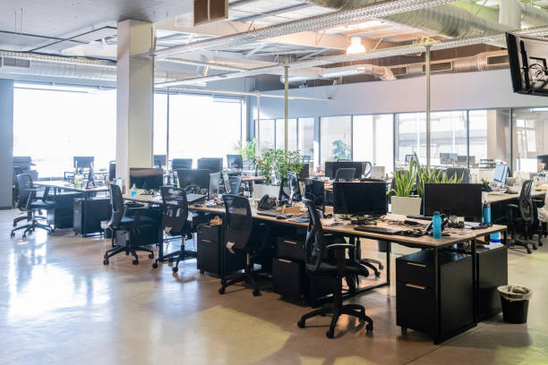 Open plan office with work stations and computers Modern office with desks and chairs, natural light coming though window, spacious work environment workplace absence stock pictures, royalty-free photos & images