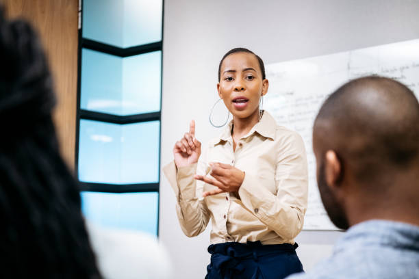 Serious young businesswoman leading colleagues in meeting Attractive female African professional her 20s gesturing with hands, manager explaining to co-workers and delegating, empowered woman in corporate environment delegating stock pictures, royalty-free photos & images