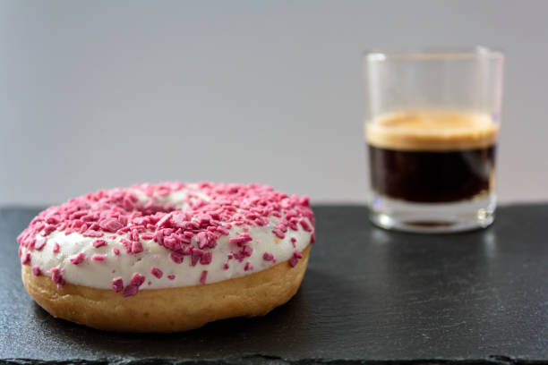 Donut with white frosting and pink sprinkles and a cup of black coffee