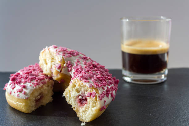 Donut with strawberry filling cut in half and a cup of espresso coffee