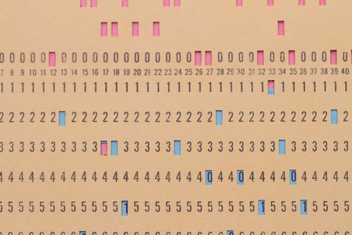 Vintage computer punch card data input documents.  Programming instructions were input into computers by punching holes in cards to spell out the software code. A yellow card with holes punched is laid over red and blue cards.