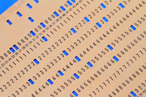 Vintage computer punch card data input documents.  Programming instructions were input into computers by punching holes in cards to spell out the software code. A yellow card with holes punched is laid over a blue card.