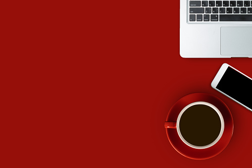 Flat lay red desk with laptop, smartphone and a red cup of black coffee, top view with copy space