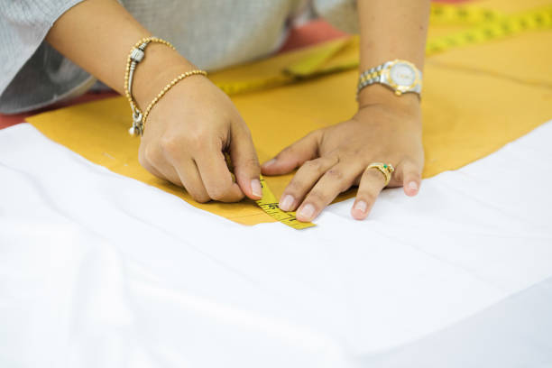Close-up on female hands measuring sewing pattern on white fabric.