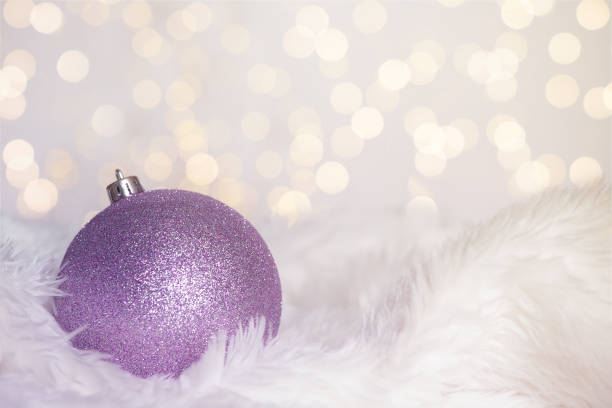 Single purple glittering Christmas ornament on white fur with lighted background