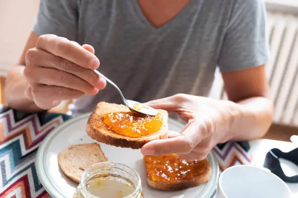 Photo of young man spreading jam on a toast