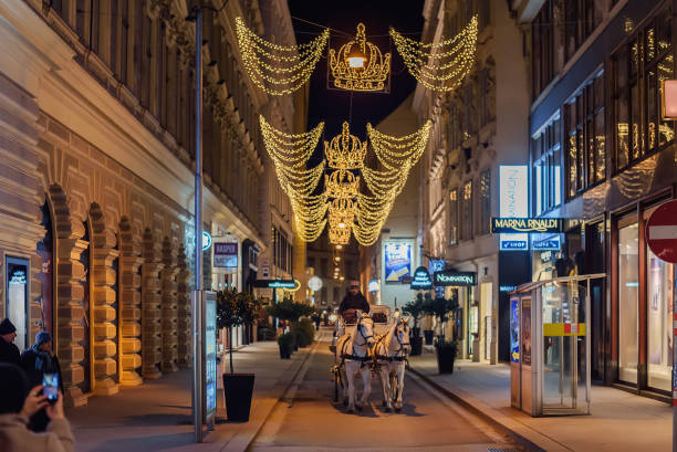 Vienna, Austria - December 24, 2017. Christmas street decorated with illuminated crowns, and horse-drawn carriage with a coachman. Fiacre with white horses and driver ride down central Xmas Vienna.