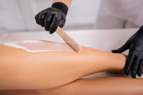 istock Master in hair removal holding legs of her client while putting wax on 1073859356