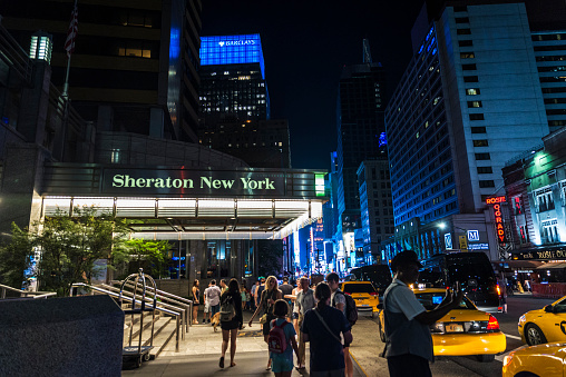 New York City, USA - July 30, 2018: Sheraton New York Times Square Hotel at night on Seventh Avenue (7th Avenue) next to Times Square with people around and a bellboy in Manhattan in New York City, USA