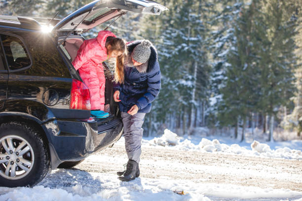 Family with father mother and two adorable little kids standing joking holding ski by the open car trunk