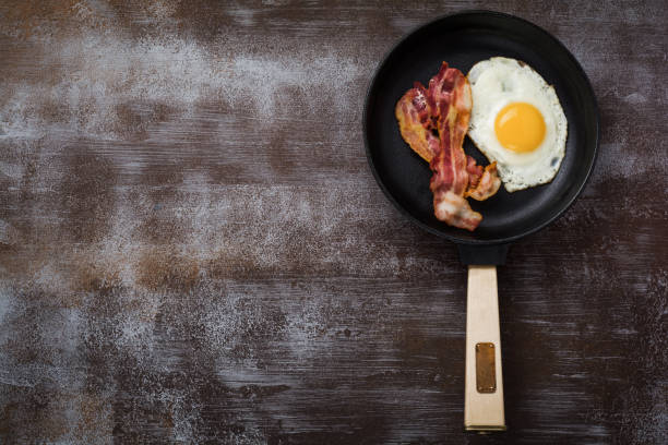 istock Traditional English breakfast with fried eggs and bacon in cast iron pan on dark concrete background. Top view. 1073880280