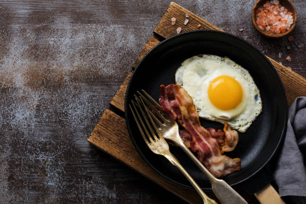 istock Traditional English breakfast with fried eggs and bacon in cast iron pan on dark concrete background. Top view. 1073881184