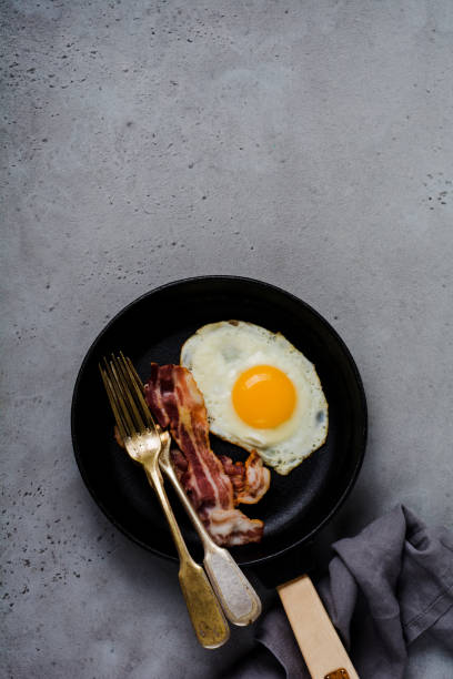 tradicional desayuno inglés con huevos fritos y bacon en hierro fundido cacerola en viejo fondo de hormigón gris. vista superior. - photography metal traditional culture full fotografías e imágenes de stock