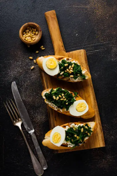 Fried spinach, egg and pine nuts sandwiches on brown vintage old concretebackground. Delicious healthy breakfast or snack. Top view.