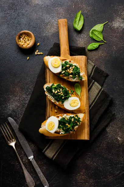 Fried spinach, egg and pine nuts sandwiches on brown vintage old concretebackground. Delicious healthy breakfast or snack. Top view.
