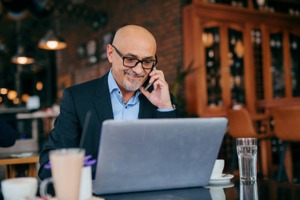 istock Senior businessman using smart phone and laptop while sitting in cafe. Coffee on the table. 1073904780