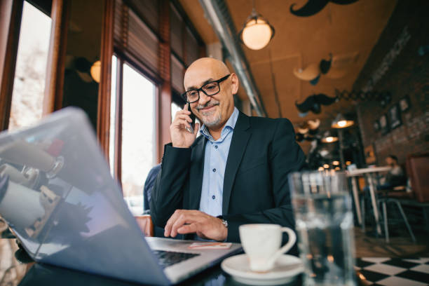 istock Senior businessman using smart phone and laptop while sitting in cafe. Coffee on the table. 1073905338