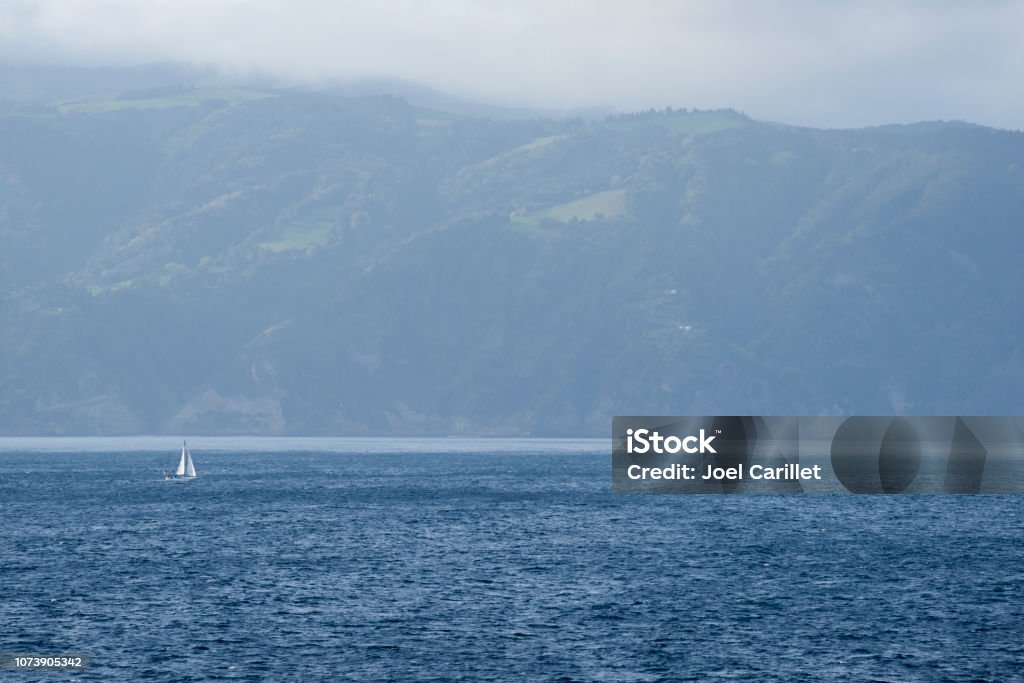 Sailing in the Atlantic ocean off coast of São Miguel, Azores A sailboat sails in the Atlantic Ocean off the mountainous coast of São Miguel in the Azores. Atlantic Islands Stock Photo