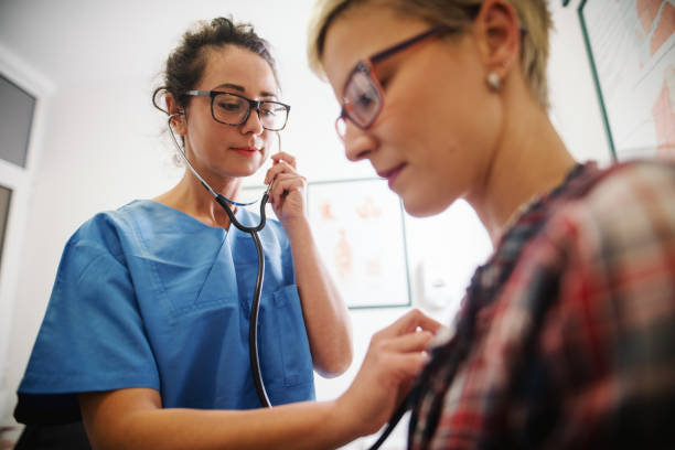 mediana edad doctora usando el estetoscopio para examinar el paciente. - escuchando el latido del corazón fotografías e imágenes de stock