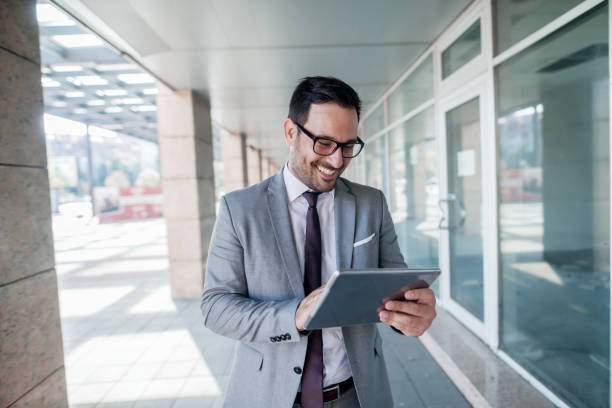 istock Happy businessman using tablet while standing in front of business center. 1073911614