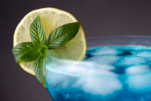 Detail of blue lagoon cocktail with blue curacao liqueur, vodka, lemon juice and soda, decorated with lemon slice and mint leaves. Selective focus on the mint leaves