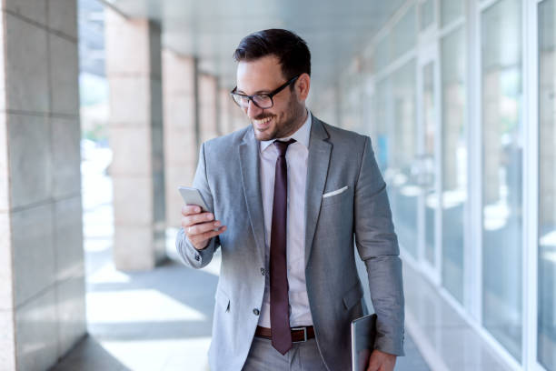 istock Smiling Caucasian businessman using smart phone and holding tablet in other hand while walking outdoors. 1073914568