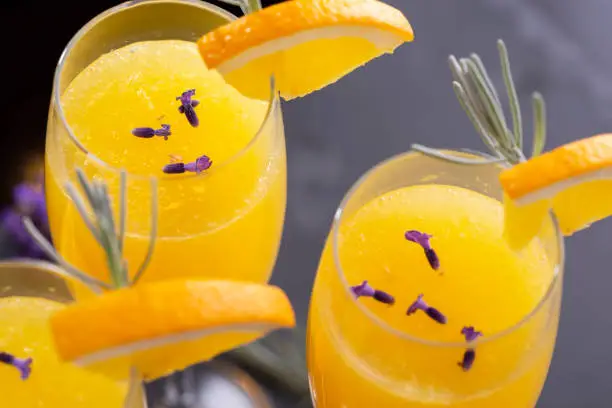 High angle view of mimosa cocktails with orange juice and champagne decorated with lavender leaves and flowers and orange slices. Focus on the lavender flowers in the glass