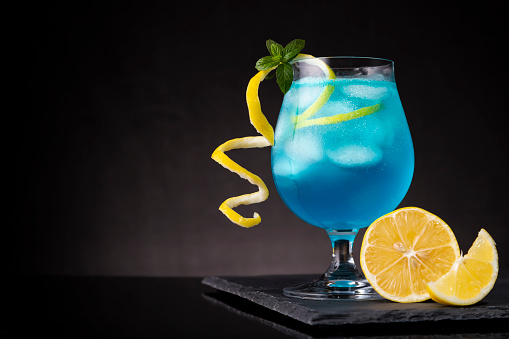 Blue lagoon cocktail with blue curacao liqueur, vodka, lemon juice and soda, decorated with lemon slice and mint leaves. Selective focus on the mint leaves