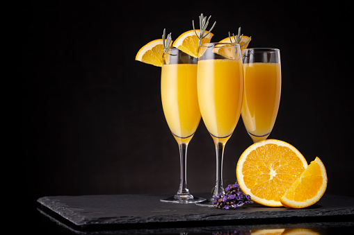 Mimosa cocktails in champagne glasses with orange juice and sparkling wine decorated with lavender leaves and orange slices