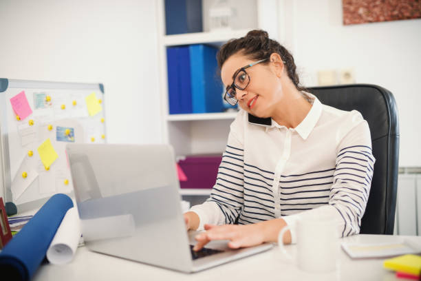 Busy assistant talking on the phone and using laptop. Office interior.
