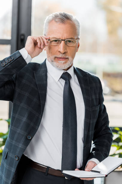 istock confident mature businessman adjusting eyeglasses and looking at camera 1073919250