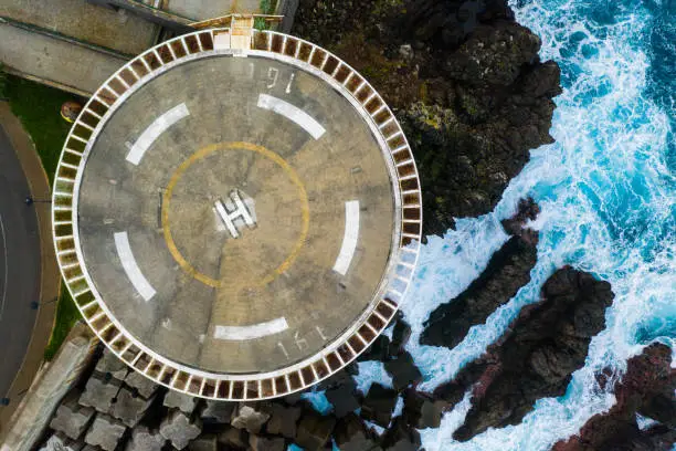 Helicopter landing pad on the edge of the cliff by the ocean waves.